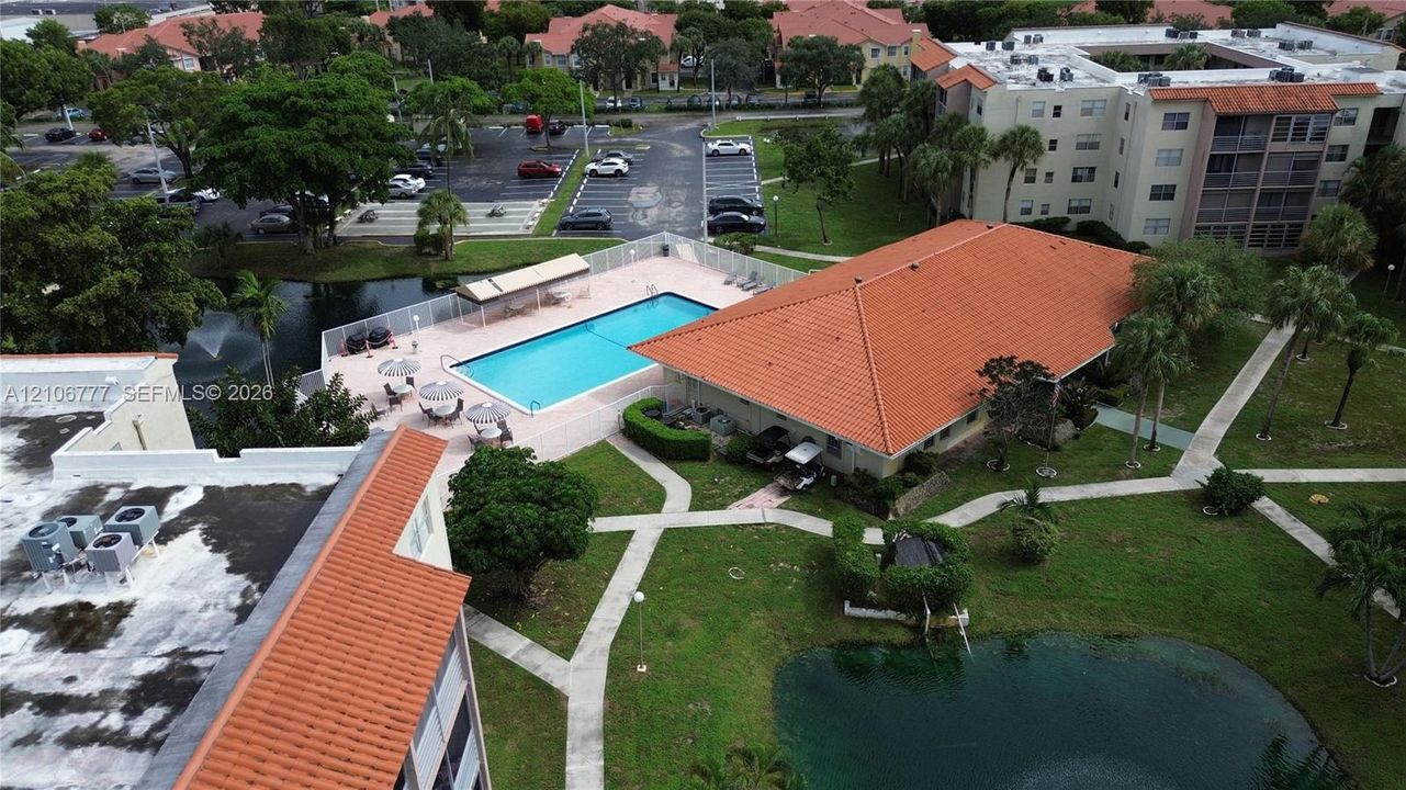 Community swimming pool with a tiled deck, terracotta-style roof systems, landscaped grounds, and a water feature