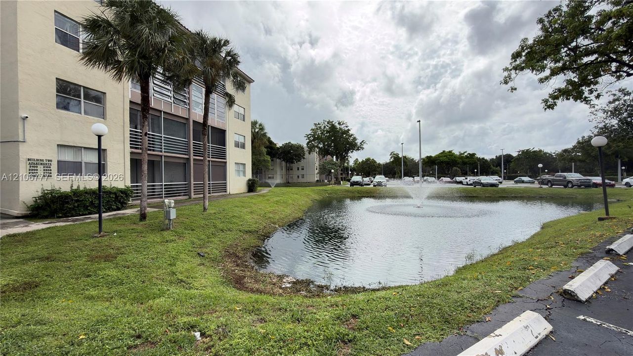 Multi-story stucco exterior featuring screened balconies, landscaped grounds, and a central water fountain pond