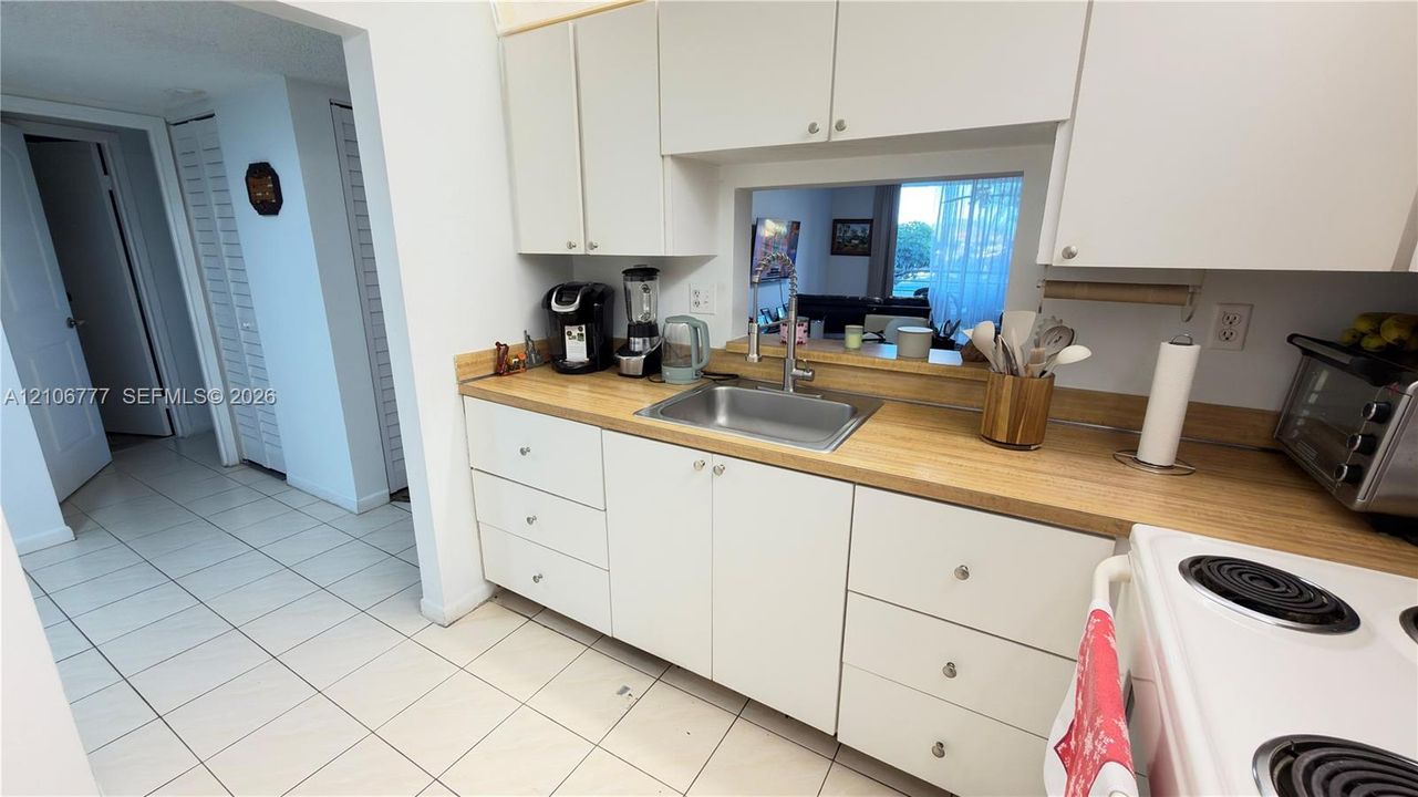 Kitchen featuring white cabinetry, light-toned countertop, stainless steel sink with a goose-neck faucet, and tile flooring