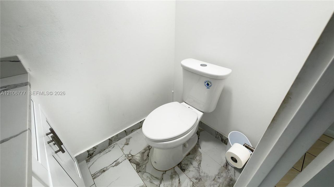 Dual-flush toilet paired with stone-finish floor tiling featuring distinct veining, white cabinetry with dark metal hardware, and a matching stone-finish countertop