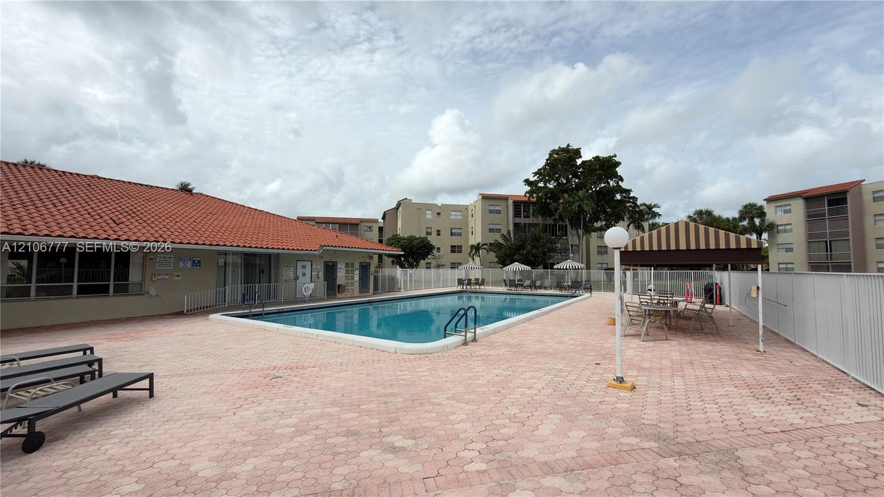 Rectangular swimming pool featuring a concrete deck, red tile roofing, and a metal-framed shaded pavilion