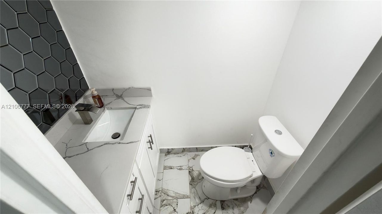 White vanity with a veined stone-finish countertop, rectangular under-mount sink, matte-finish faucet, charcoal hexagon-tile backsplash, and large-format porcelain tile flooring
