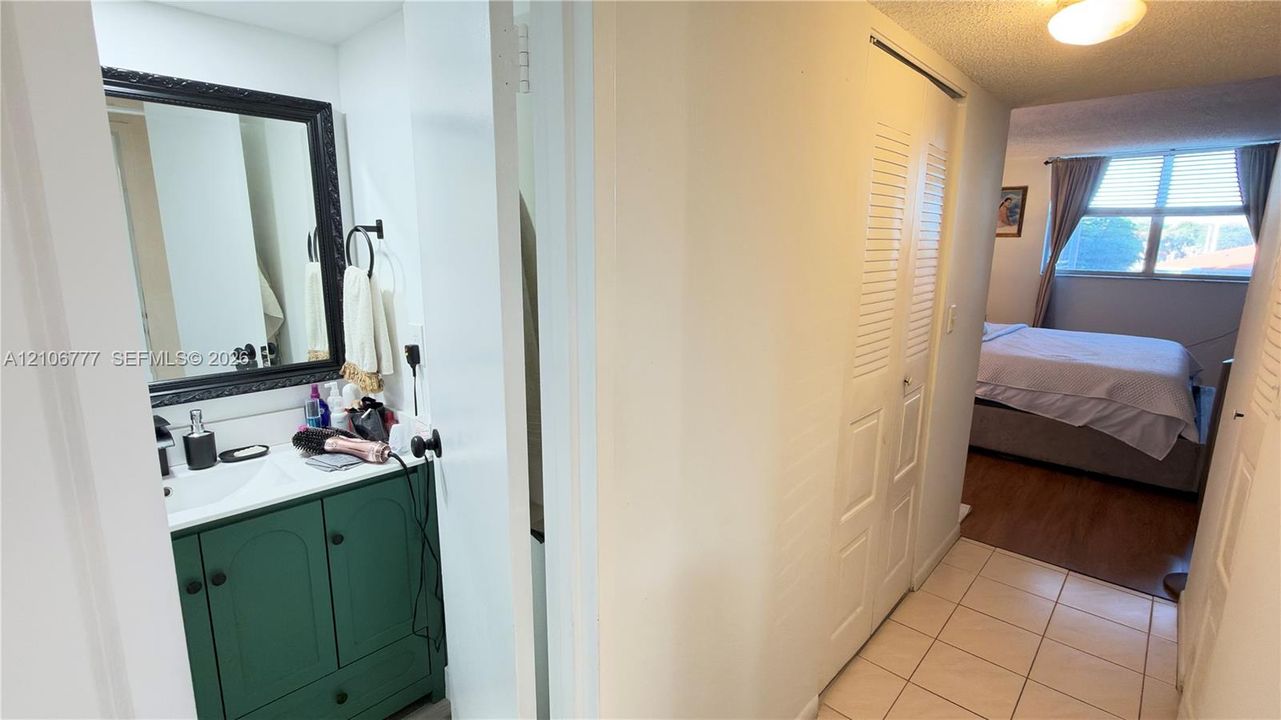 Bathroom vanity featuring a green cabinetry base, white countertop with integrated sink, and dark-toned framed mirror, complemented by ceramic floor tiling and louvered closet doors