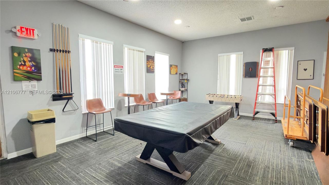 Spacious room featuring neutral wall paint, carpet tile flooring, and multiple windows with vertical blinds