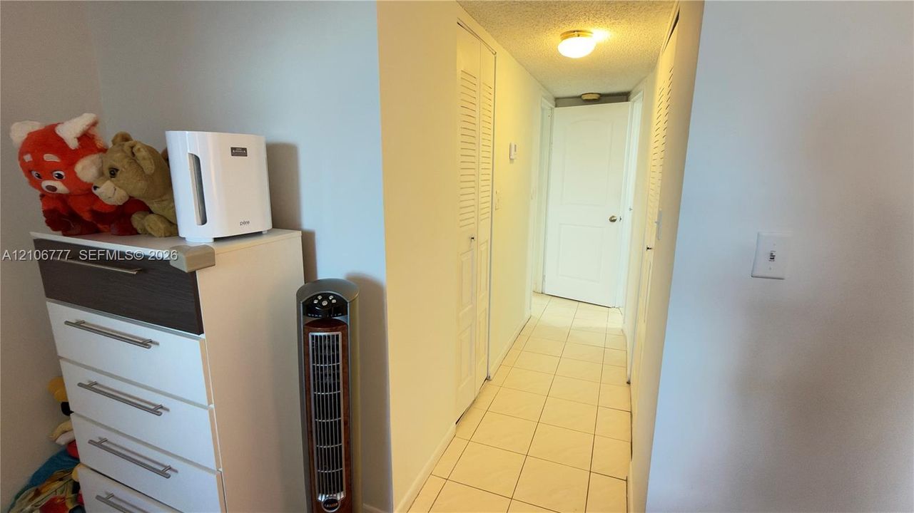 Interior hallway featuring tile flooring, ceiling-mounted lighting, and two sets of louvered bifold closet doors