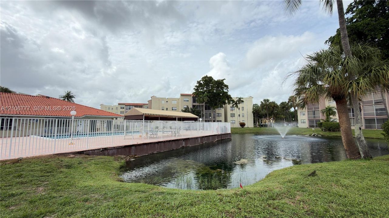Community pool featuring a terra-cotta tile roof, paved deck, protective perimeter fencing, and a waterfront location with an integrated fountain