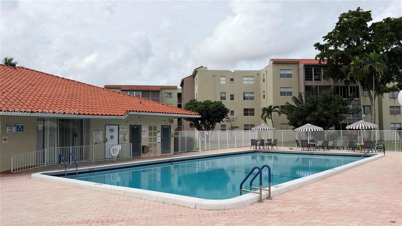 In-ground swimming pool featuring a concrete deck, metal safety fencing, and a red tile roof clubhouse