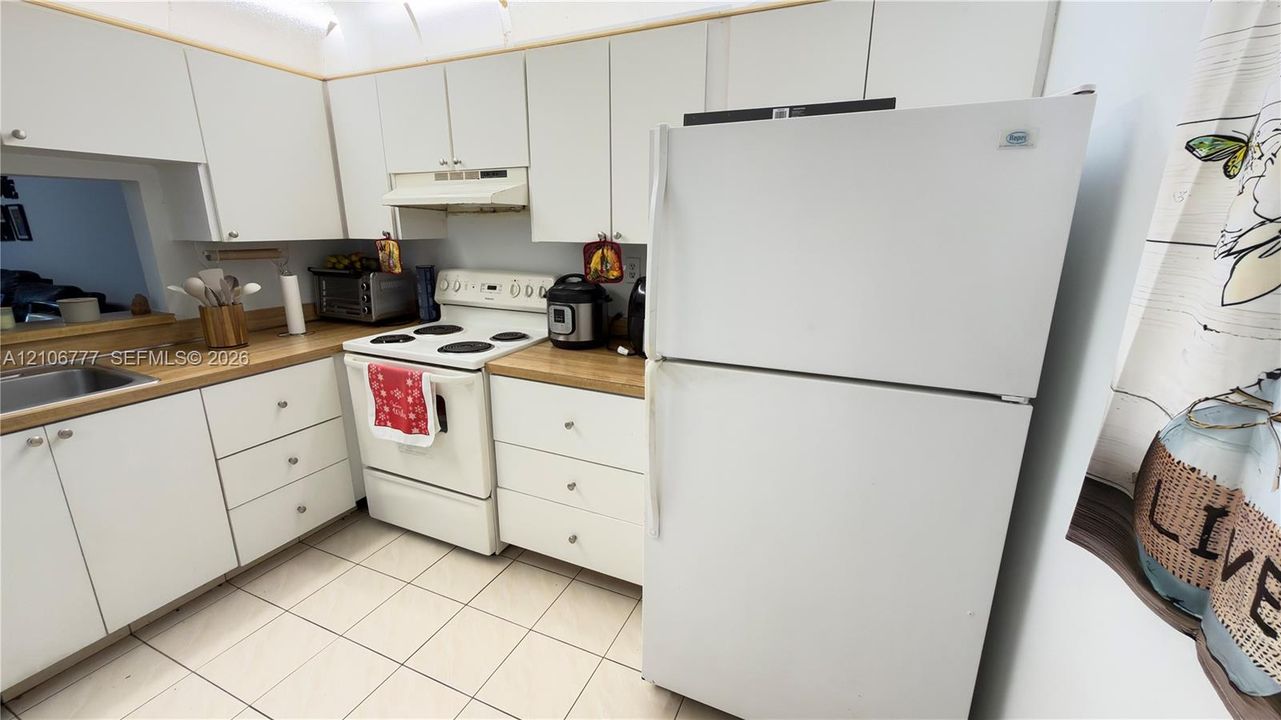 Kitchen featuring white cabinetry, wood-finish countertops, tile flooring, and a range with a built-in hood