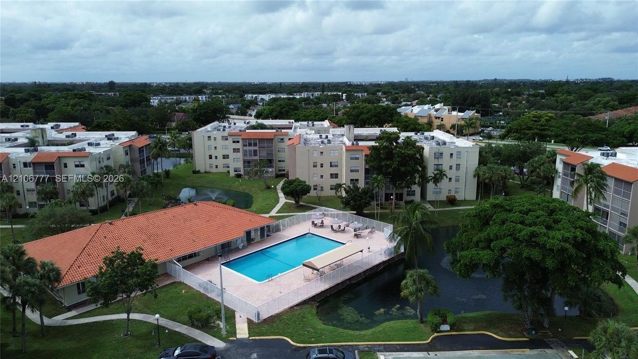 Community swimming pool featuring a concrete deck and enclosure, set within landscaped grounds containing a pond