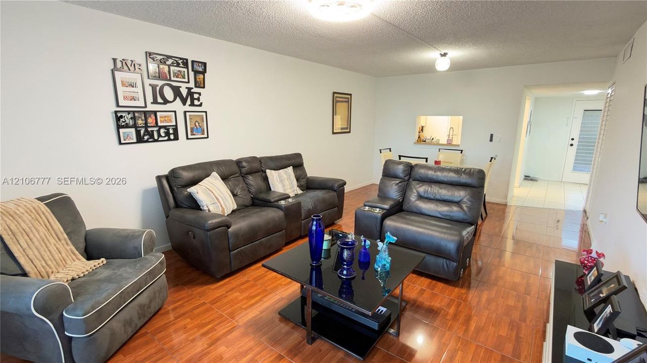 Open-concept interior featuring wood-finish tile flooring, ceiling-mounted light fixtures, and a pass-through kitchen opening