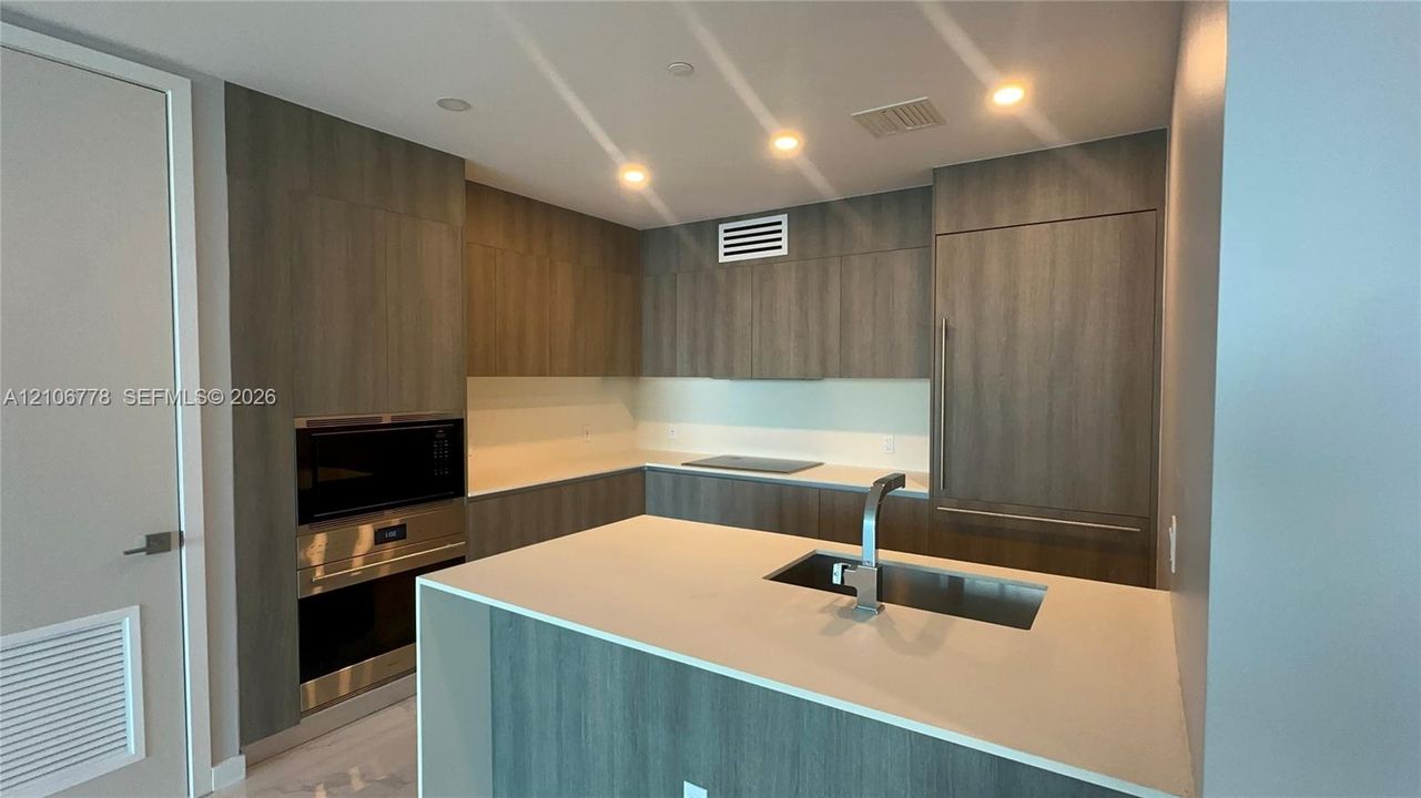 Modern kitchen featuring wood-finish cabinetry, integrated built-in appliances, a center island with an undermount sink, and recessed lighting