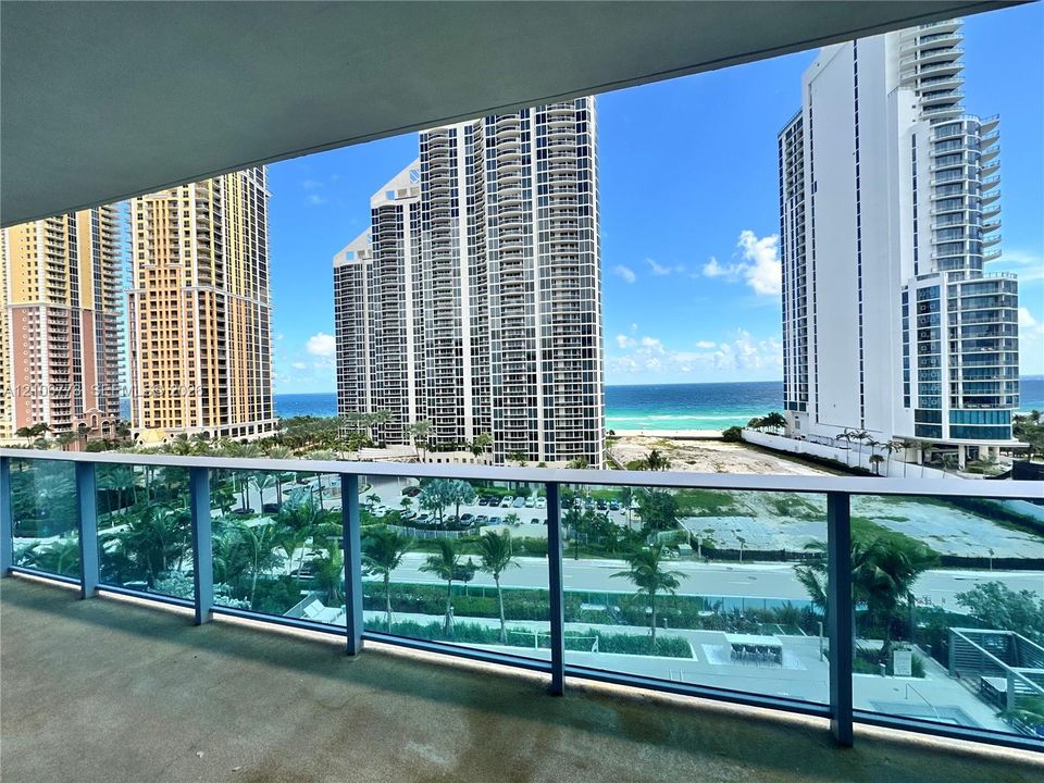 Balcony with transparent glass railing, offering ocean scenery, urban high-rise buildings, and palm trees