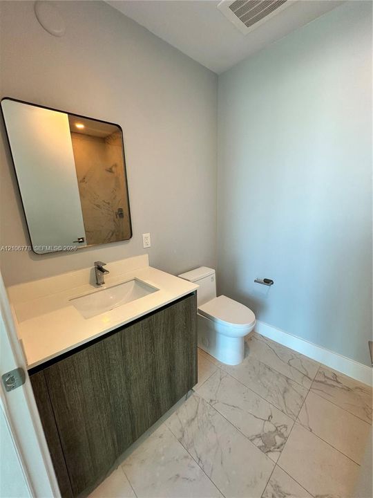 Modern vanity with a rectangular sink, stone-finish countertop, and wood-texture cabinetry, complemented by large-format tile flooring and a wall-mounted mirror with a black frame
