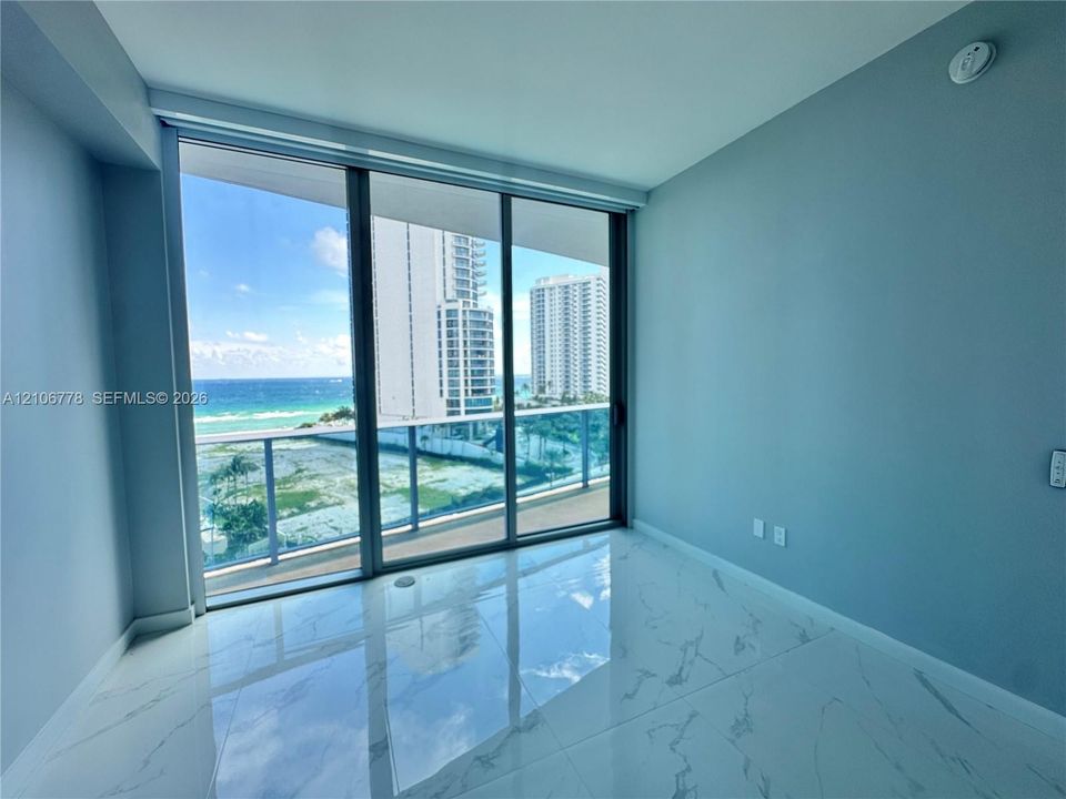 Floor-to-ceiling sliding glass doors, polished stone-finish tile flooring, and a glass-paneled balcony railing overlooking the ocean