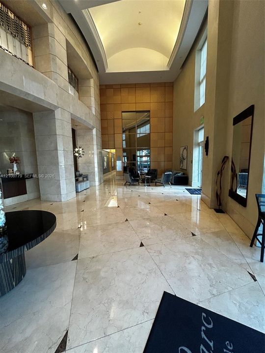 Grand lobby featuring polished stone flooring with geometric insets, expansive multi-story ceilings, large-scale stone-clad pillars, and a decorative barrel-vaulted ceiling architectural element