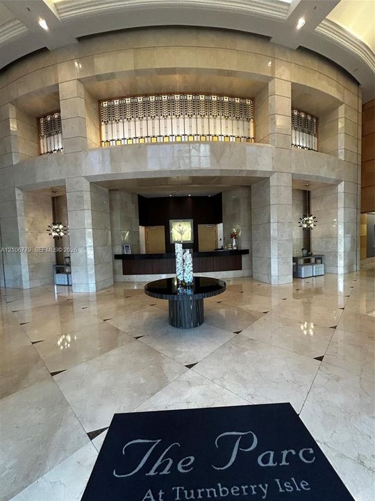 Grand lobby featuring floor-to-ceiling stone wall cladding, polished stone tile flooring with decorative inlay, a multi-level architectural recessed facade, and ornate metal grille detailing