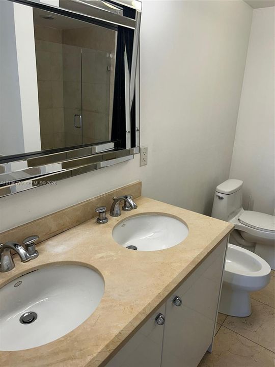 Dual-sink vanity with a stone countertop, metal-finish widespread faucets, a large framed mirror, and tile flooring