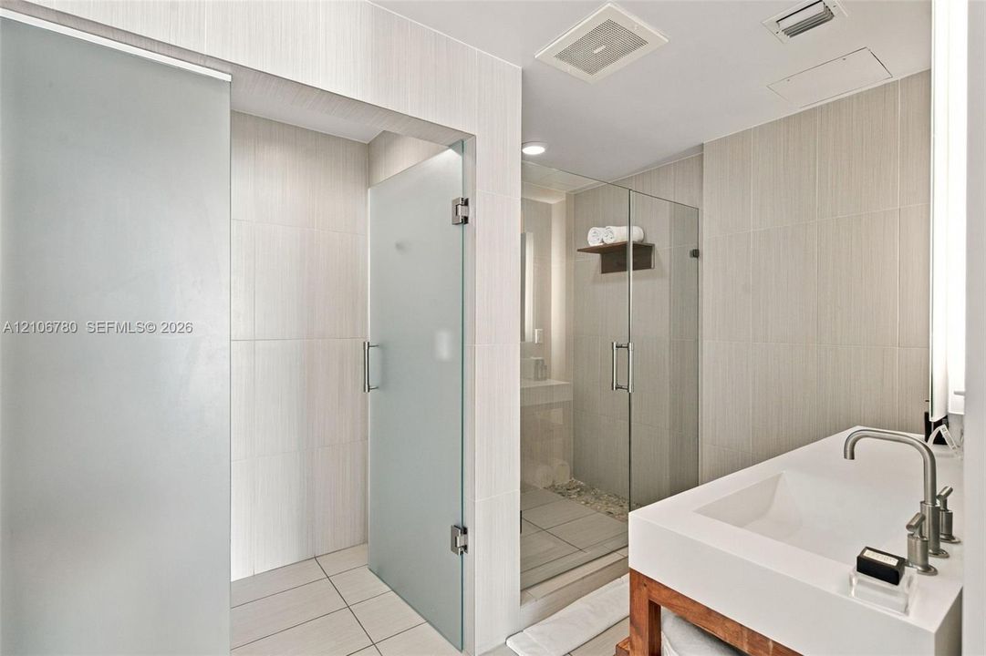 Custom vanity featuring a thick countertop and integrated rectangular sink, paired with a glass-enclosed shower with tiled walls and stone flooring, accented by frosted glass door panels and minimalist hardware