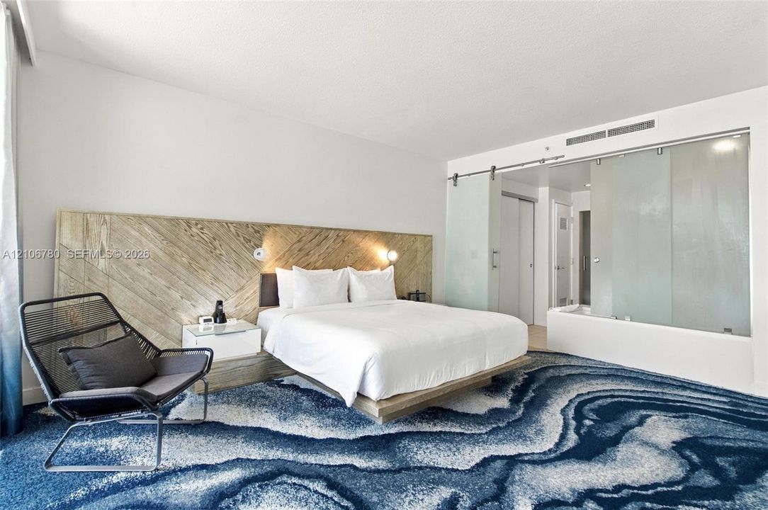 Custom built-in headboard featuring diagonal wood-finish detailing, platform bed frame, sliding frosted glass privacy panels with brushed metal hardware, and patterned wall-to-wall carpeting