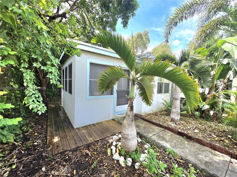 Detached structure featuring a smooth stucco exterior, screen-enclosed entrance, wood-finish decking, and stone-lined landscaping