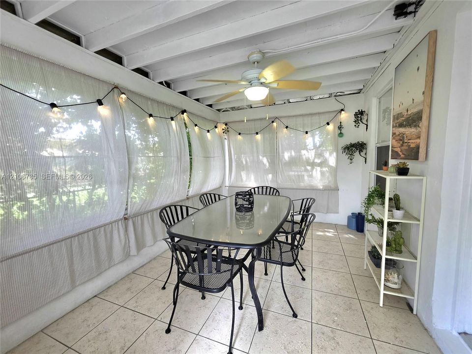 Enclosed patio featuring white exposed beam ceilings, neutral tile flooring, and a central ceiling fan