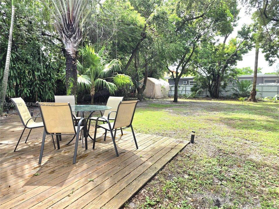 Wood-plank deck featuring mature trees, shaded lawn, and a perimeter fence