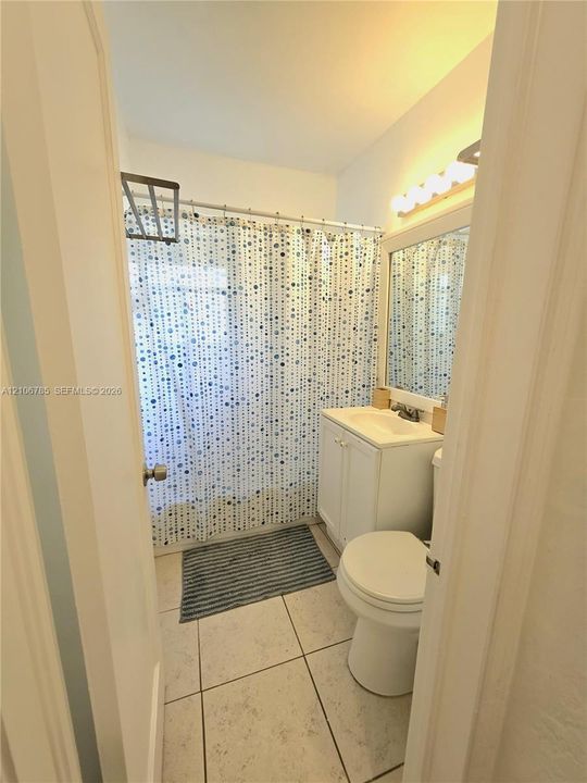 Bathroom featuring a vanity with an integrated sink, a rectangular mirror, a multi-bulb light fixture, a shower-tub combination with a wall-mounted rack, and tile flooring