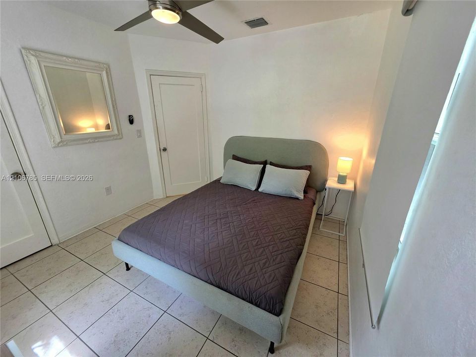 Interior space featuring neutral tile flooring, two paneled doors with metallic hardware, and a ceiling-mounted fan with an integrated light fixture