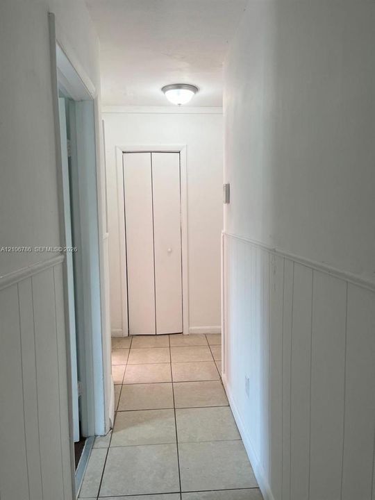 Hallway featuring tile flooring, wainscoting, and a bi-fold closet door with a flush-mount ceiling light fixture
