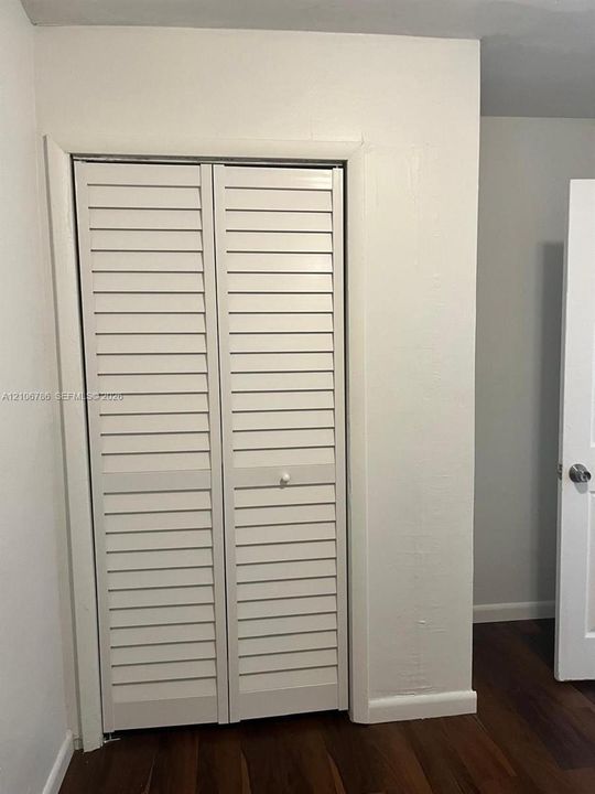 Built-in bi-fold louvered closet doors with a white finish and wood-finish flooring