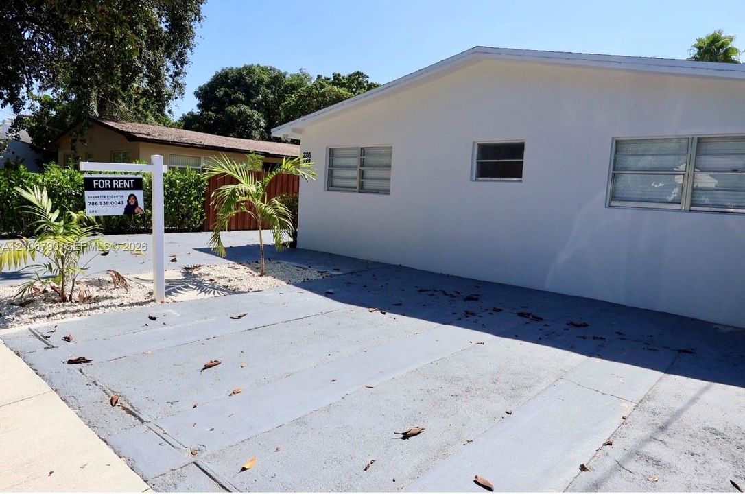Single-story exterior featuring white smooth stucco siding, louvered windows, and a paved concrete driveway