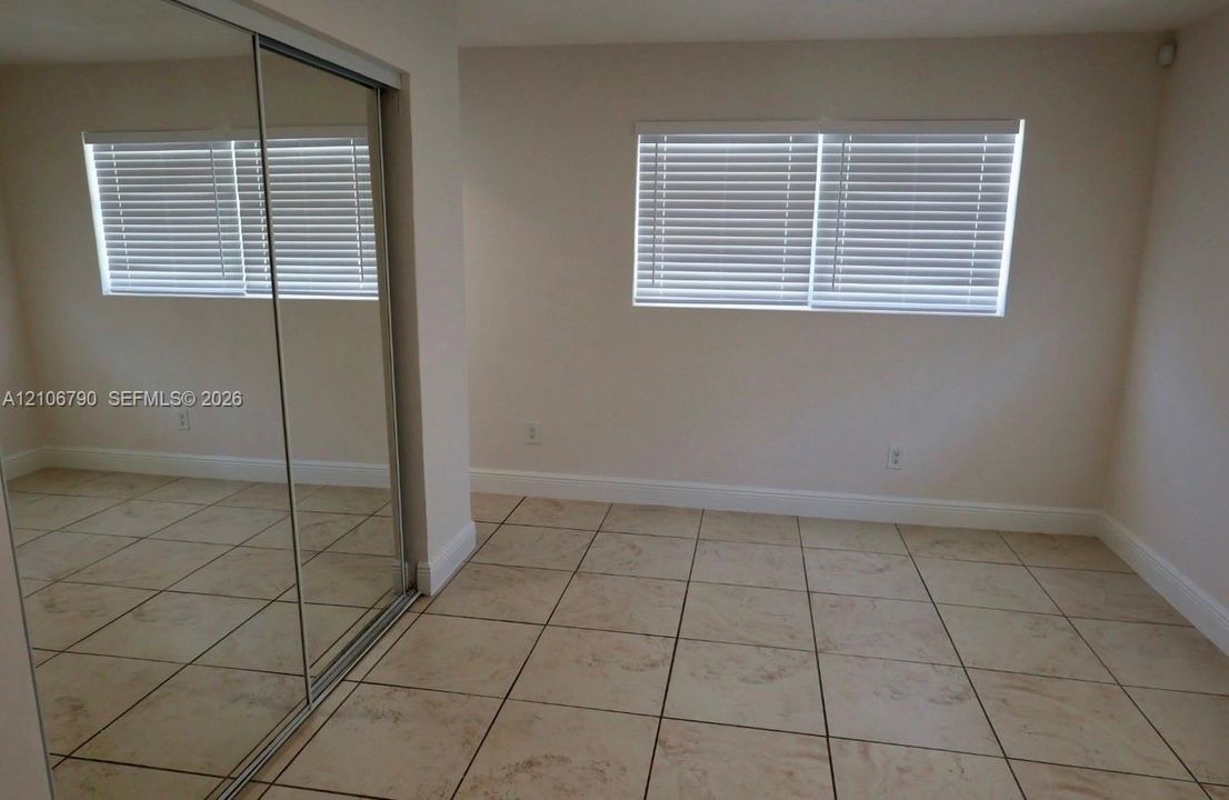Neutral tile flooring, sliding mirrored closet doors, and windows featuring horizontal blinds