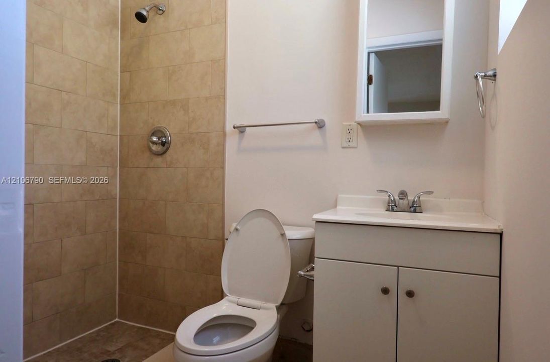 Bathroom featuring a walk-in shower with neutral tile surround, integrated sink vanity with cabinet storage, and surface-mounted medicine cabinet