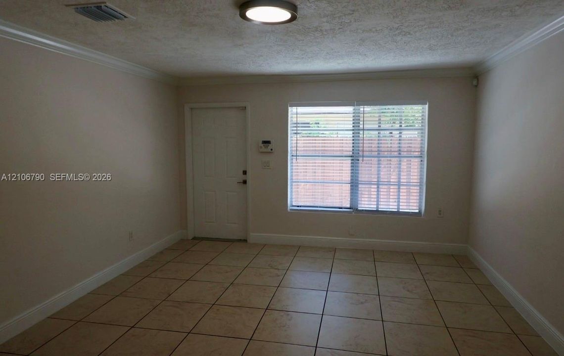 Interior space featuring neutral wall paint, tile flooring, crown molding, flush-mount ceiling lighting, and a window with horizontal blinds