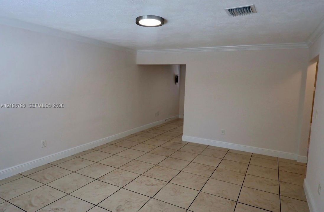 Neutral interior space featuring large-format ceramic tile flooring, crown molding, and a modern circular flush-mount ceiling light