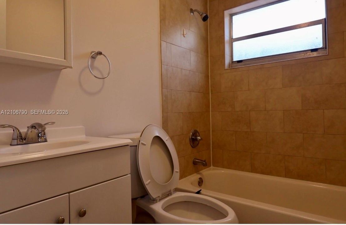 Bathroom featuring a white vanity cabinet, rectangular countertop sink with chrome hardware, tub-shower combination with floor-to-ceiling tile surround, and an integrated window