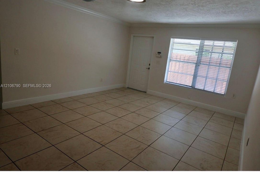 Interior space featuring light-toned ceramic tile flooring, neutral wall finishes, a multi-pane window, and a paneled exterior door