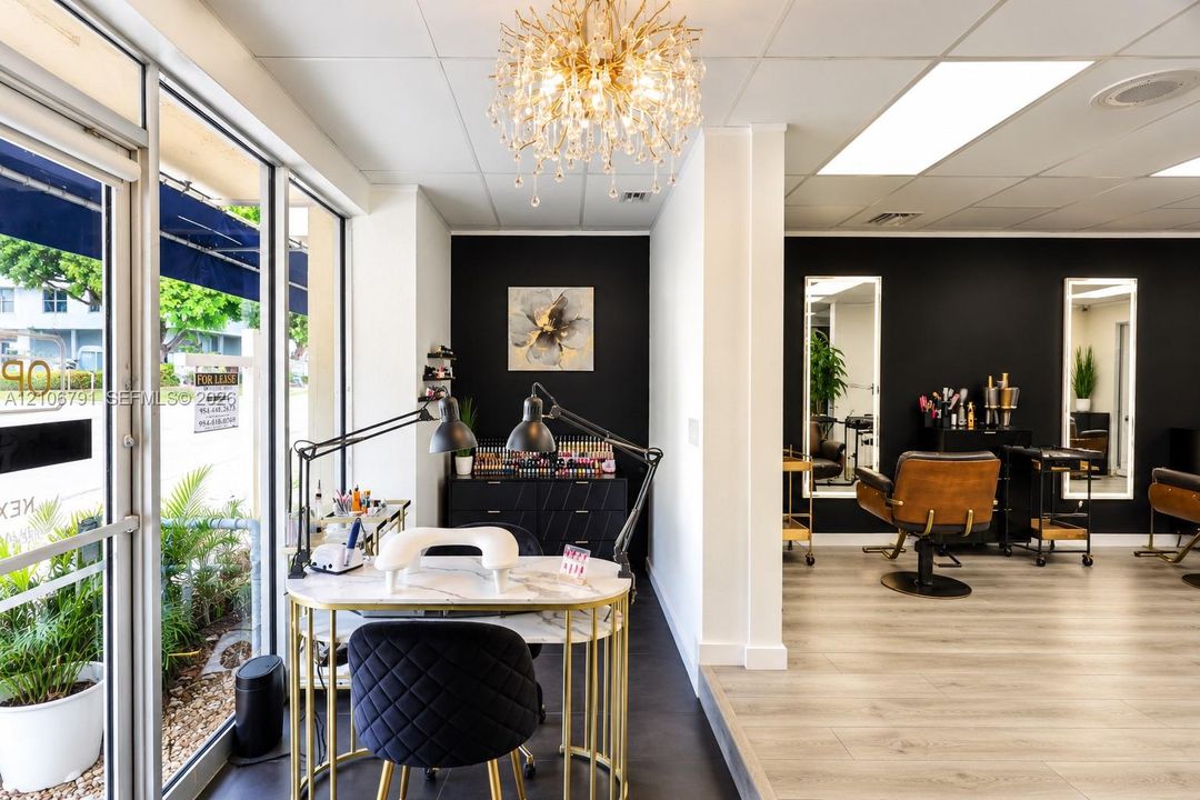 Commercial interior featuring floor-to-ceiling glass windows, wood-finish flooring, decorative crystal chandelier, and wall-mounted backlit mirrors