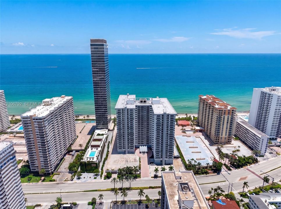 Aerial perspective of oceanfront high-rise residential properties featuring immediate proximity to the coastline, landscaped grounds, and paved parking areas