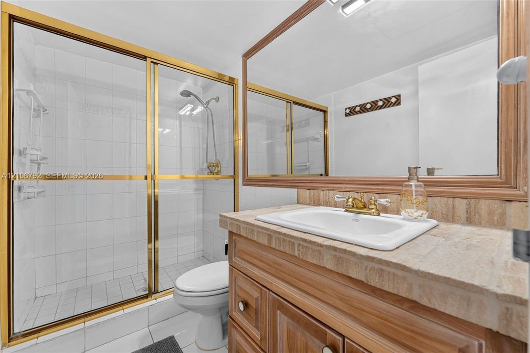 Bathroom featuring a vanity with a stone countertop, an integrated sink with gold-tone hardware, a large framed mirror, and a walk-in shower with gold-tone sliding doors and white wall tile