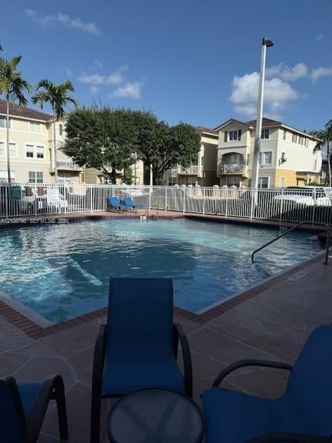 Swimming pool with flagstone-style decking, brick coping, and a metal security fence