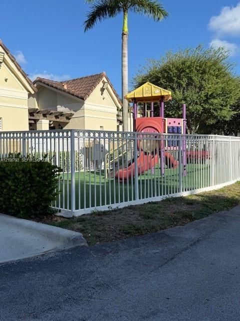 Fenced outdoor recreation area featuring synthetic turf and a structural playset