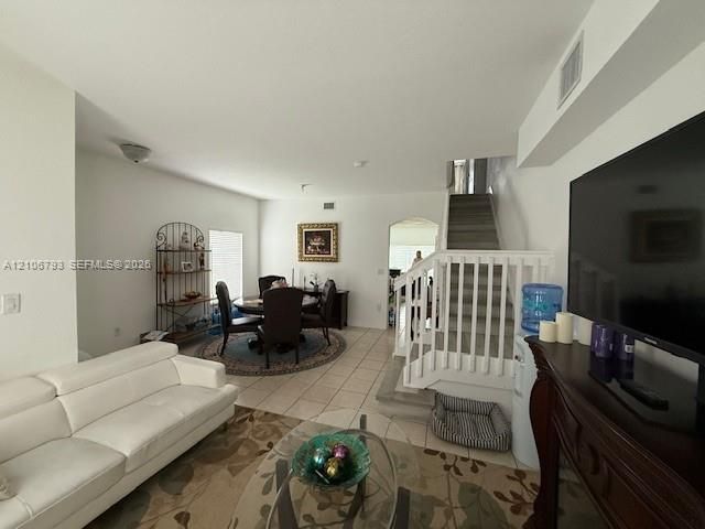 Ceramic tile flooring, staircase with white railings, arched entryway, and neutral wall tones