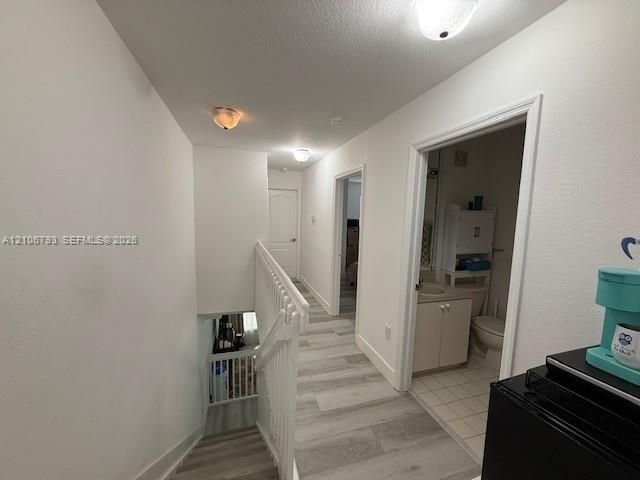 Hallway featuring wood-finish plank flooring, white interior doors, white metal stair railing, and flush-mount ceiling lighting