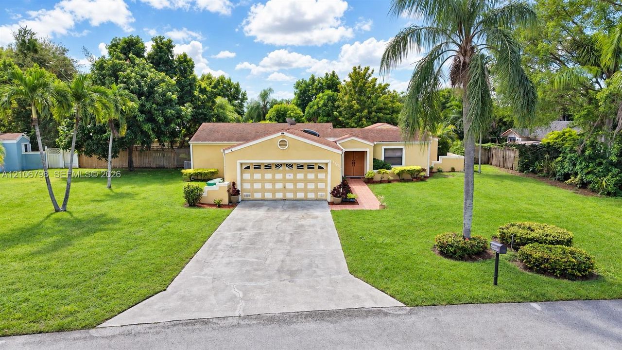 Single-story residence featuring a multi-car garage, concrete driveway, tiled roof, and extensive lawn landscaping with mature palm trees