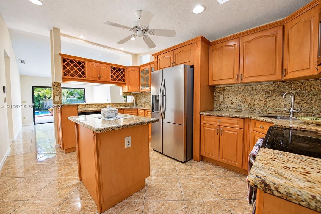 Kitchen featuring wood cabinetry, stone countertops, a central island, stainless steel refrigerator, and recessed lighting