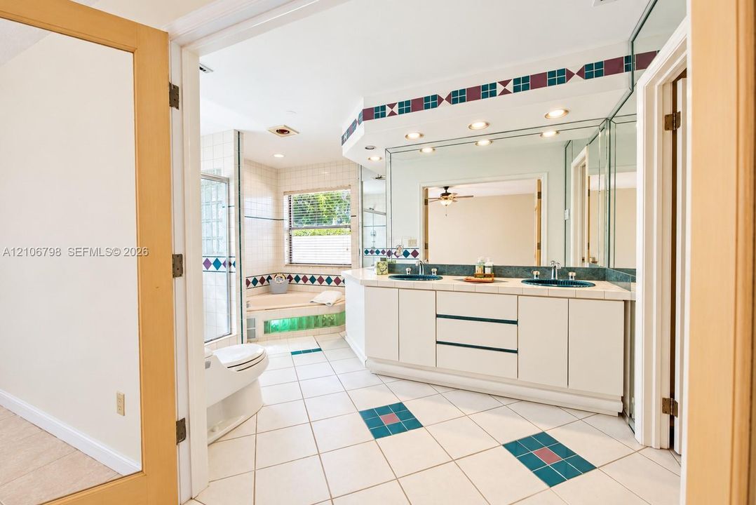 Bathroom featuring a dual-sink vanity with tile countertops, a soaking tub, recessed ceiling lighting, glass-enclosed shower, and decorative tile flooring