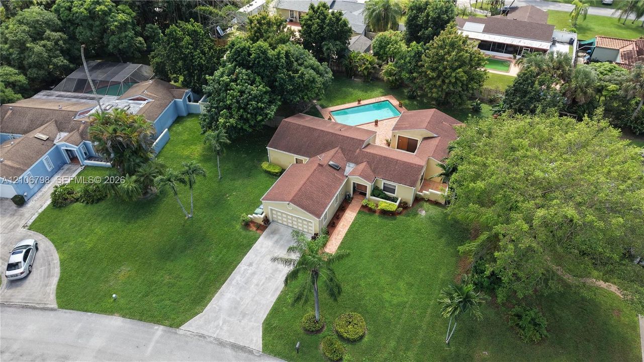 Aerial perspective of a multi-structure property featuring a swimming pool, concrete driveway, expansive lawn, and mature landscaping