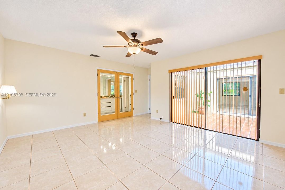 Spacious room featuring polished tile flooring, wood-framed French doors, and large sliding glass doors opening to an enclosed patio area, complemented by a central ceiling fan