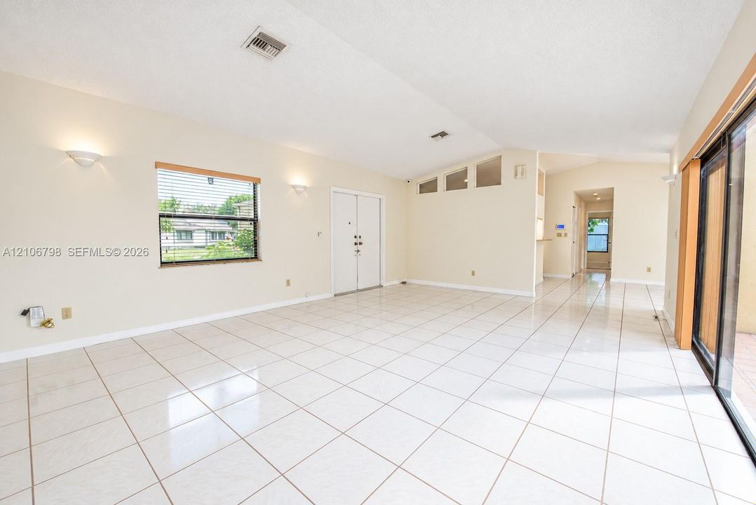 Vaulted ceilings, large-format tile flooring, dual glass-paneled entry doors, transom windows, and sliding glass patio doors